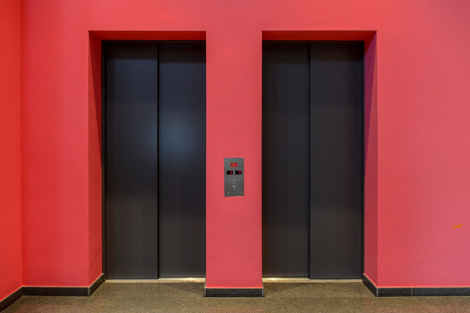 A pair of sleek modern elevator doors set against a vibrant red wall. Ideal for architectural themes.
