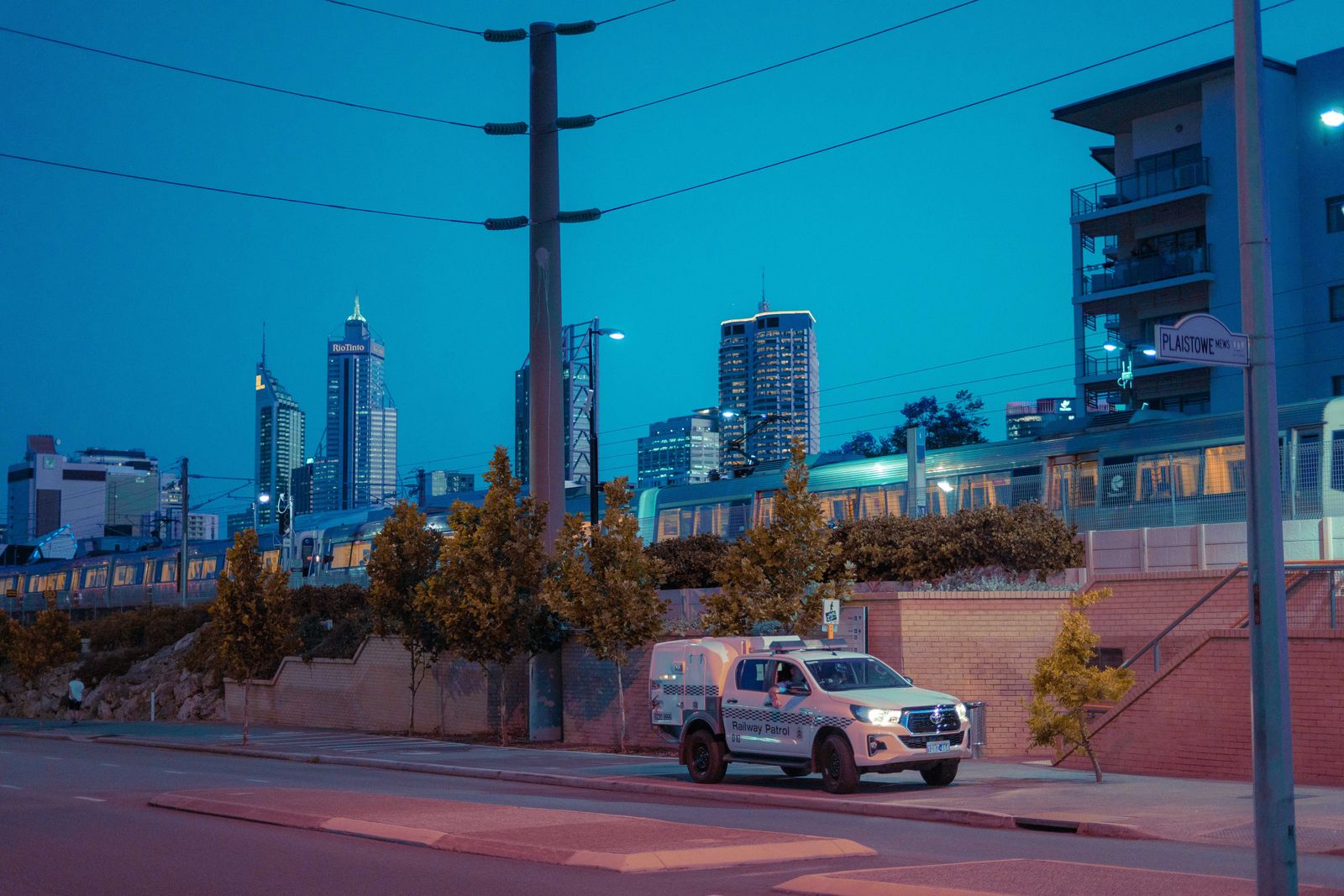 Beautiful twilight cityscape of Perth featuring a train and utility van with illuminated skyscrapers.