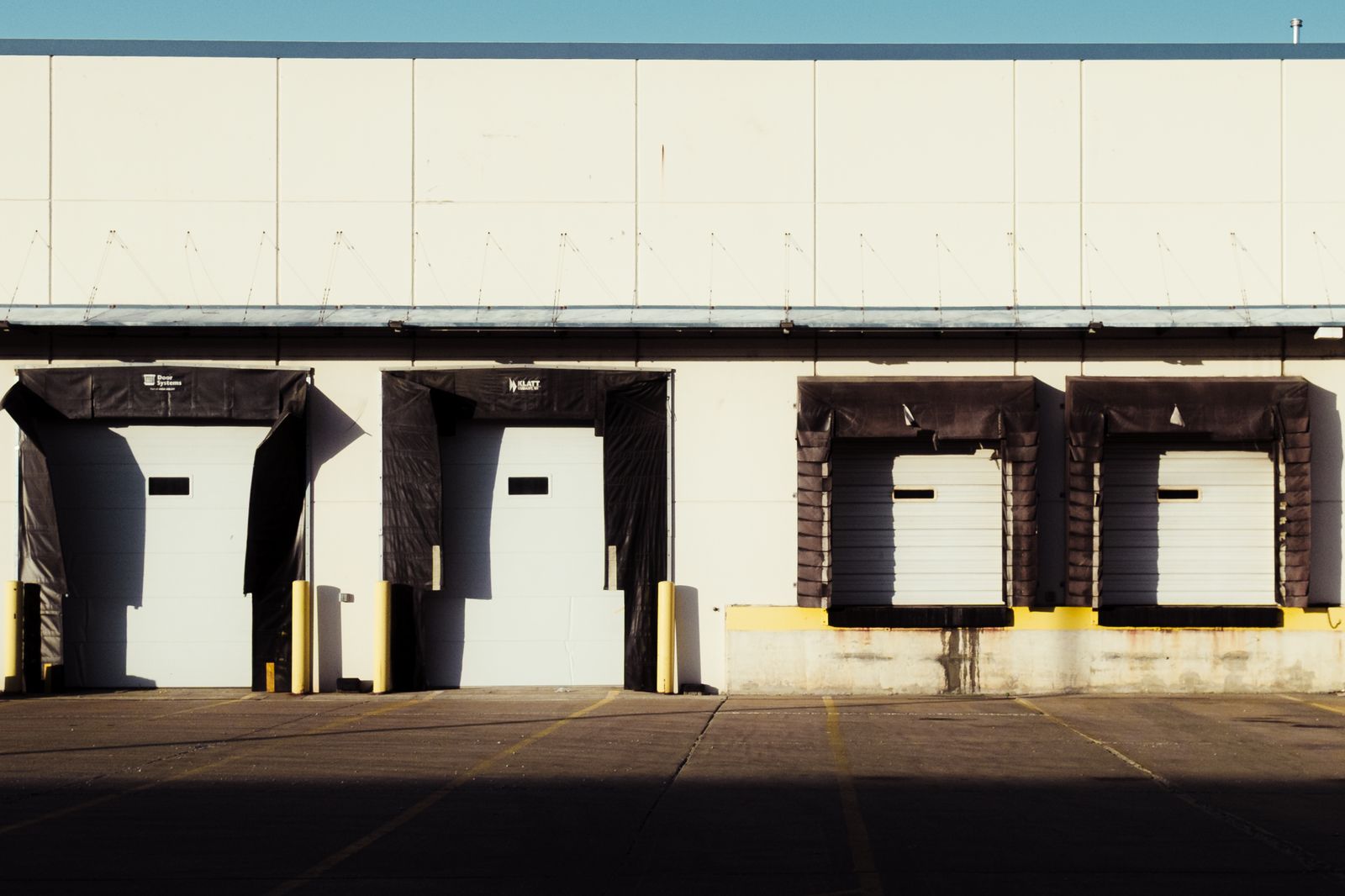 An industrial loading dock with closed bay doors, captured in bright daylight.